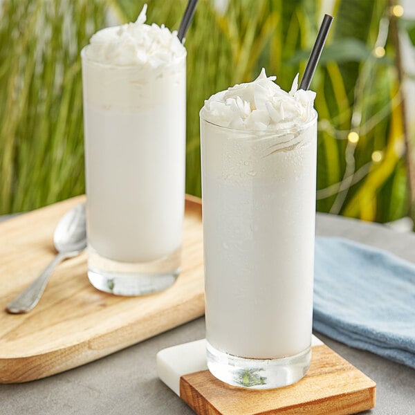 Two glasses of coconut milk with straws on a wooden tray.