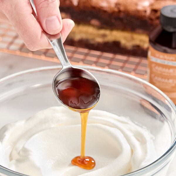 A spoonful of caramel bakery emulsion being poured into a bowl of whipped cream.
