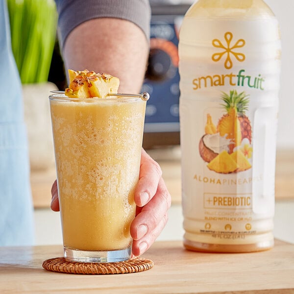 A hand holding a glass of yellow Smartfruit Aloha Pineapple beverage