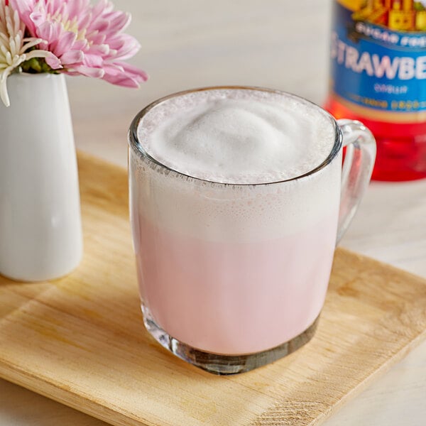 A glass cup of pink liquid with foam on top.