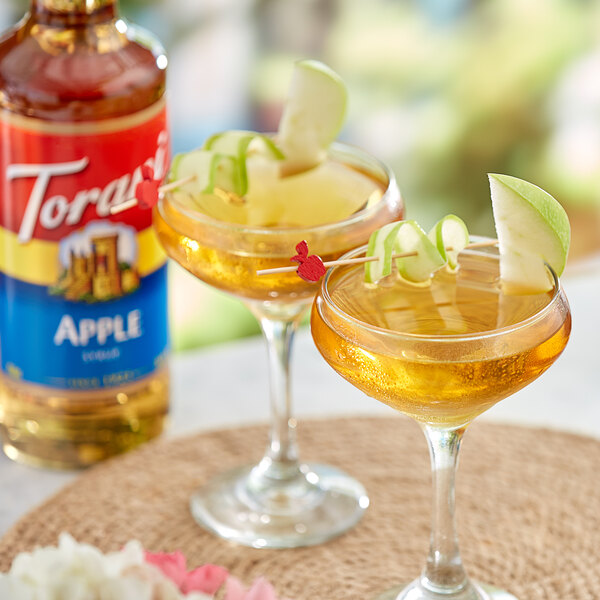 Two glasses of apple-flavored liquid with apple slices on top.