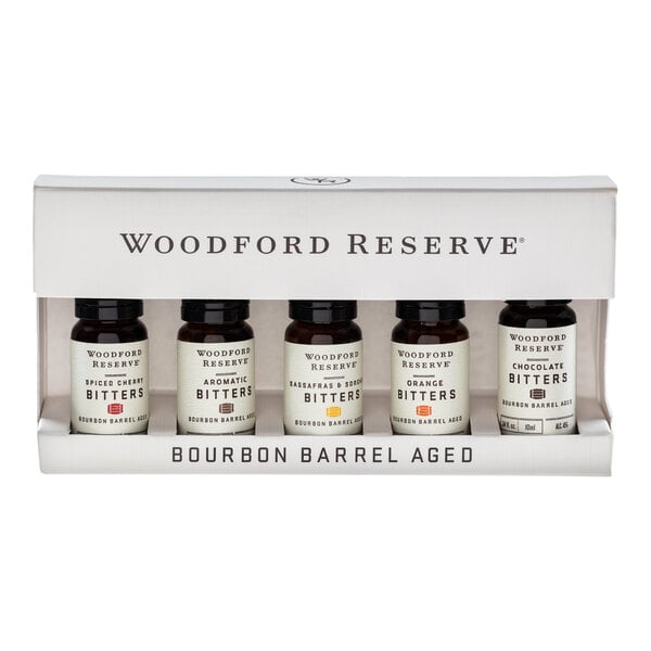 A set of five small bottles labeled "Woodford Reserve Bitters" in a white display box with the text "Bourbon Barrel Aged."