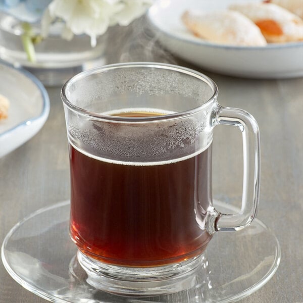 A glass mug of Caffe de Aroma French Roast coffee on a saucer with cookies.