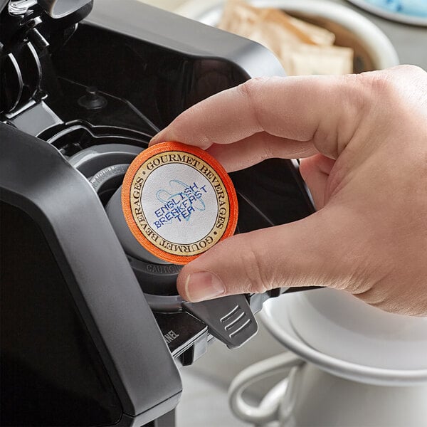 A hand holding a round orange and white label for Caffe de Aroma English Breakfast Tea.