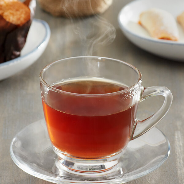 A glass cup of Caffe de Aroma English Breakfast tea on a saucer.