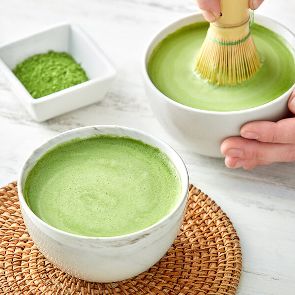 A person using a bamboo whisk to mix Jade Leaf Ceremonial Matcha into a bowl.