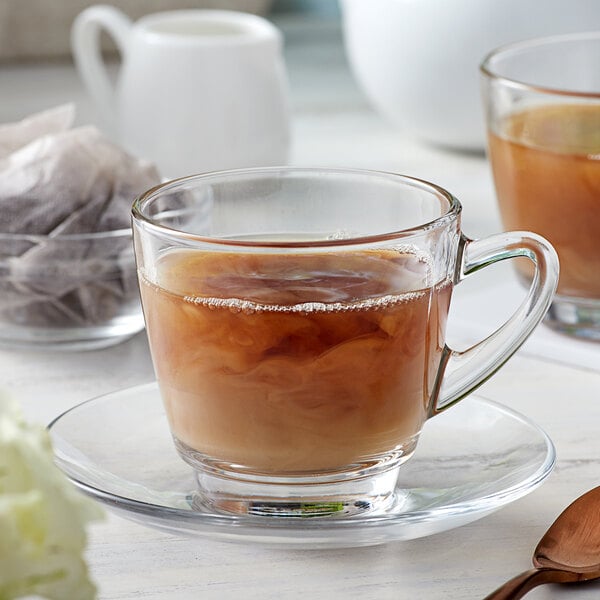 A glass cup of Bossen Hojicha Green Tea on a saucer with a spoon.