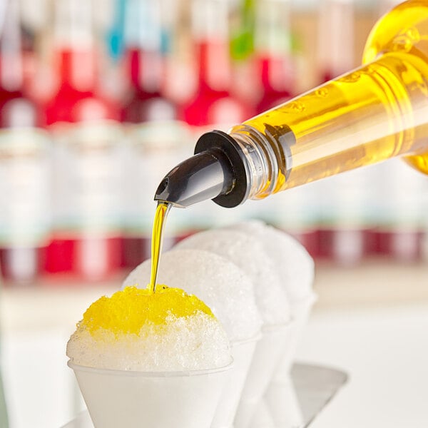 A bottle of yellow mango syrup being poured onto a cup of shaved ice.