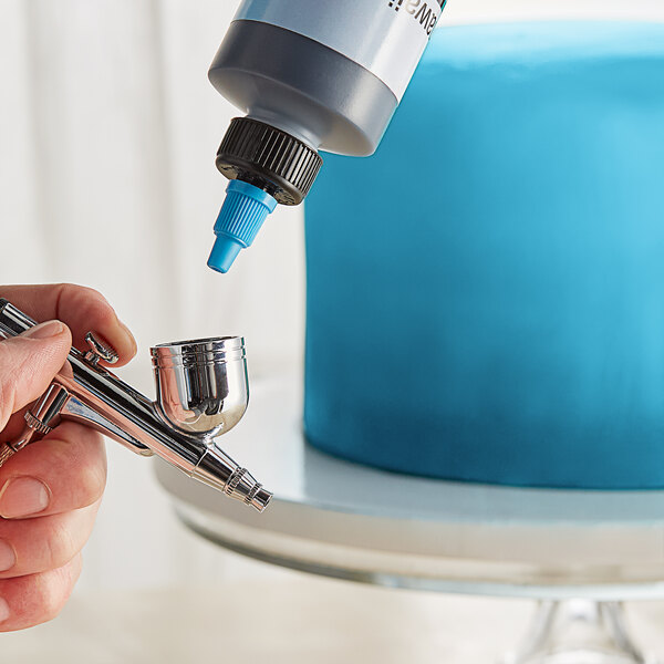 A hand using a Chefmaster Hawaiian Blue airbrush to color a cake blue.