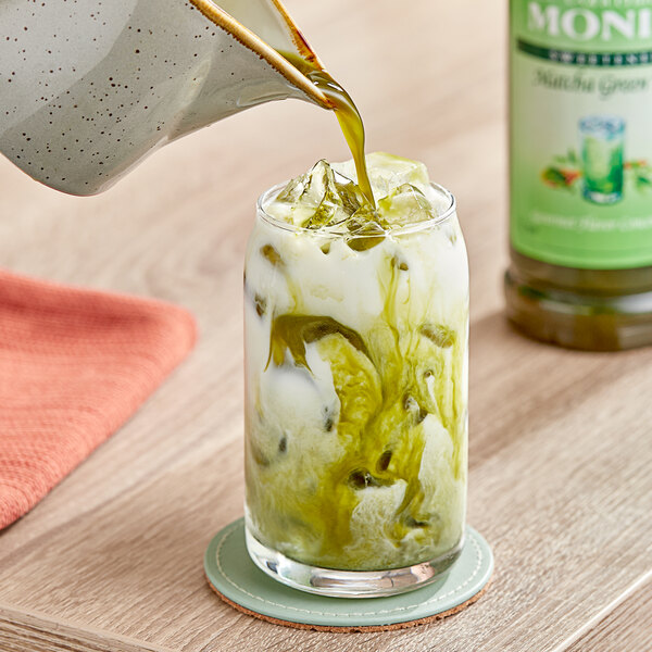 A person pouring Monin Matcha Green Tea concentrate into a glass on a table.