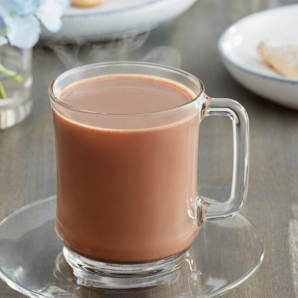 A glass mug of hot chocolate on a white plate.