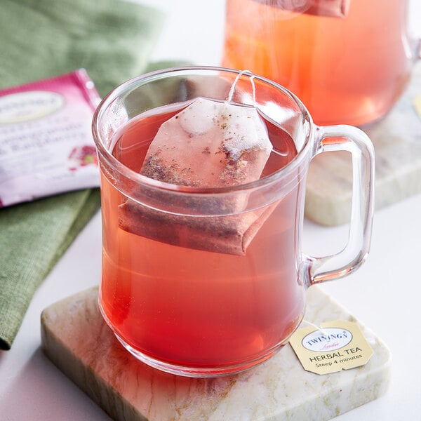 A glass mug of Twinings Pomegranate & Raspberry Herbal Tea with a tea bag in it.