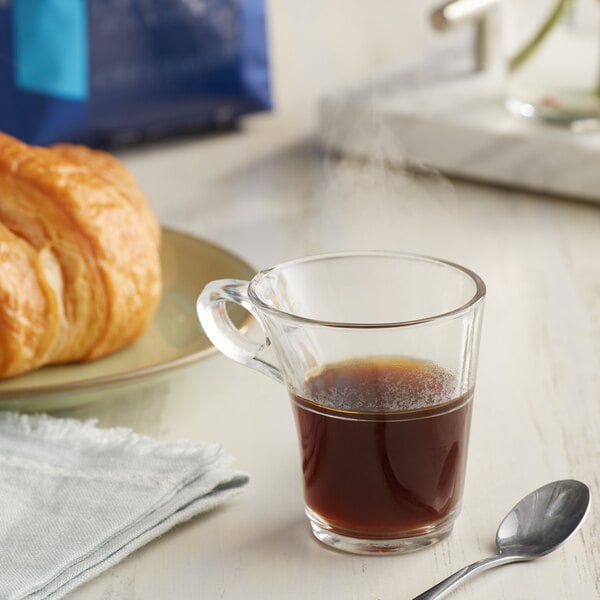 A cup of Lavazza Dek decaf espresso with a croissant on a table.