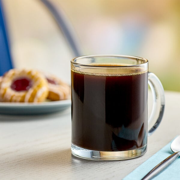 A glass mug filled with Cafe Bustelo espresso coffee on a saucer with a donut.