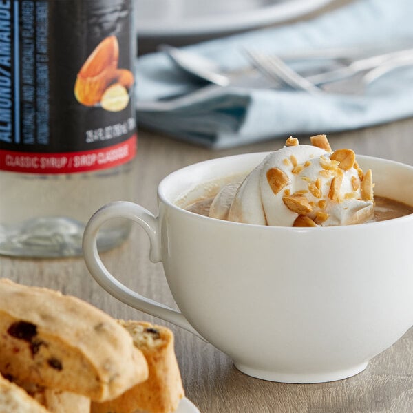 A cup of coffee with whipped cream and almonds with a bottle of DaVinci Gourmet Classic Almond Flavoring Syrup on a table.