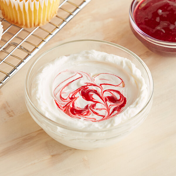 A bowl of whipped cream with red swirls on top of it next to a cupcake liner.