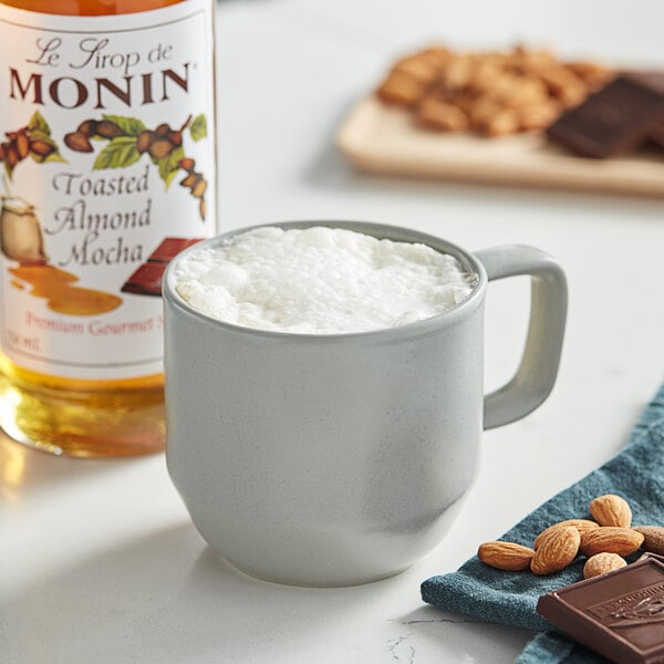 A cup of coffee with Monin Toasted Almond Mocha syrup next to nuts.