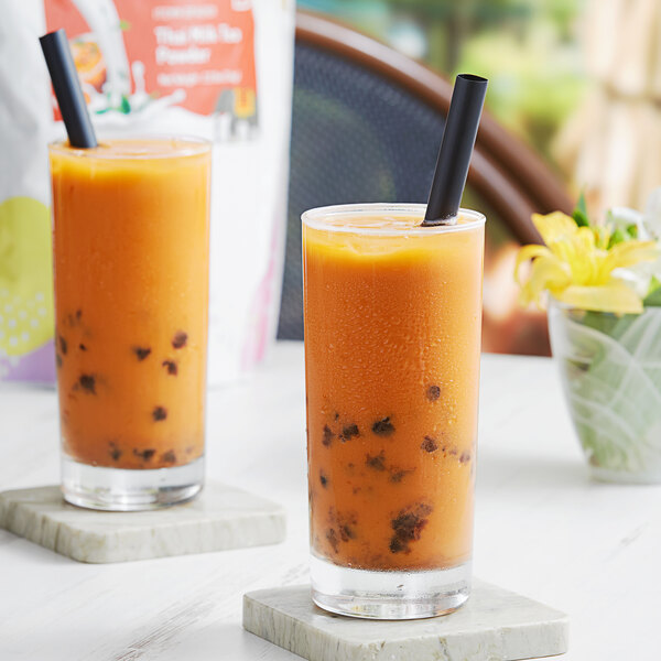 Two glasses of orange Thai tea with straws on a table.