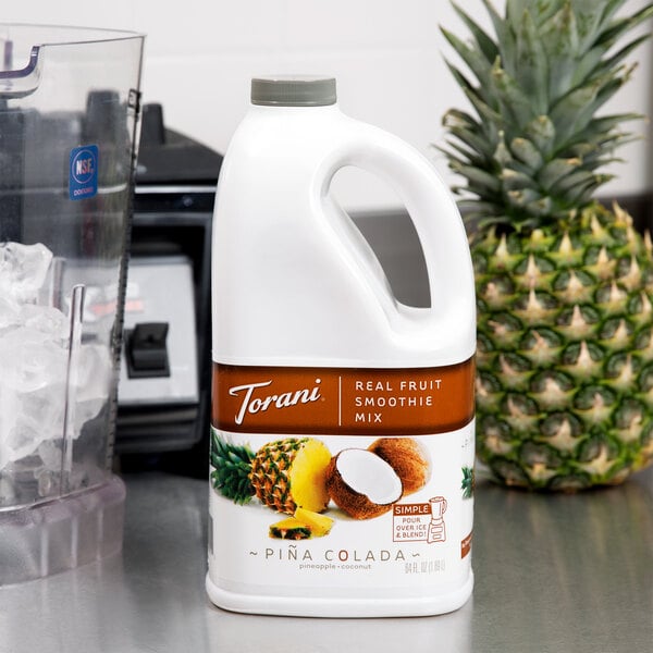 A white plastic jug of Torani Pina Colada Fruit Smoothie Mix next to a blender.