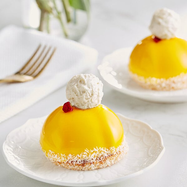 Two yellow desserts on white plates with a white ball on top.