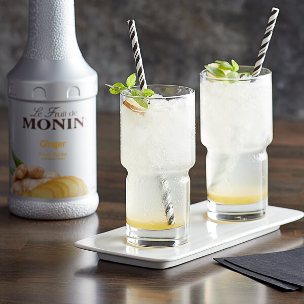 A tray with two glasses of Monin ginger fruit puree with straws and mint leaves.