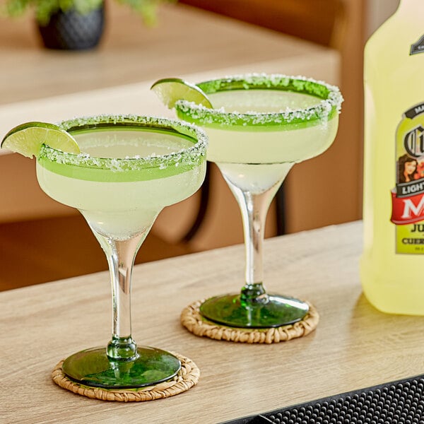 Two margaritas with lime rims and lime wedges next to a bottle of Jose Cuervo Light Margarita Mix.