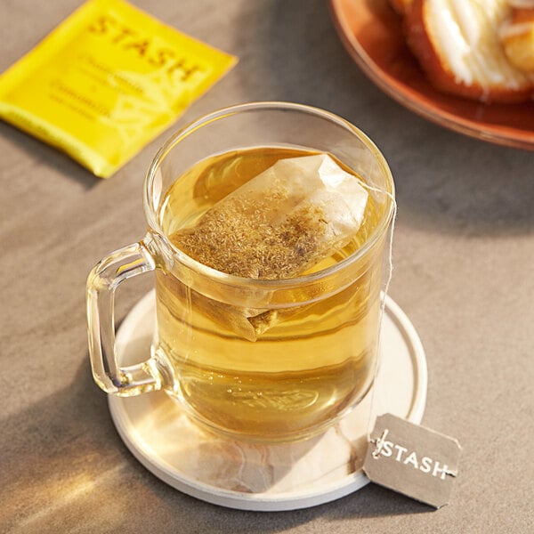 A glass mug of Stash chamomile tea with a bag of tea in it on a table.