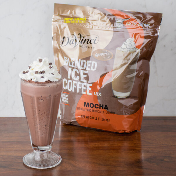 A glass of mocha milkshake with whipped cream and a bag of brown DaVinci Gourmet mocha mix.