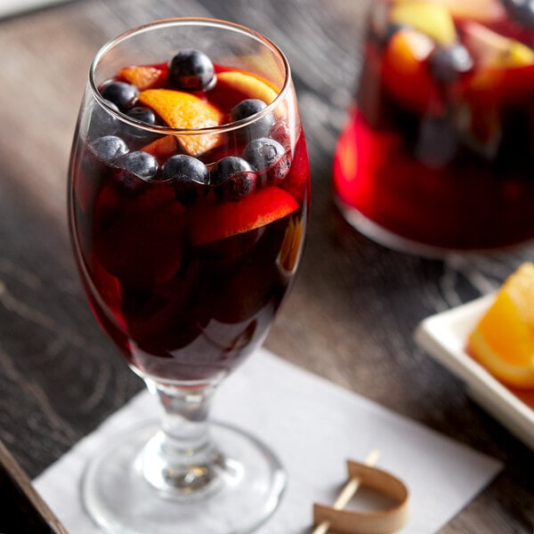 A glass of red drink with a spoon and fruit.