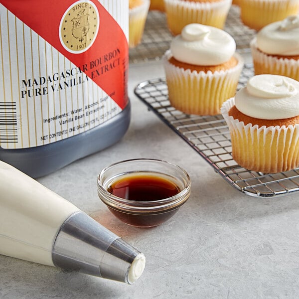 A cupcake with white frosting and a bottle of brown liquid next to it.