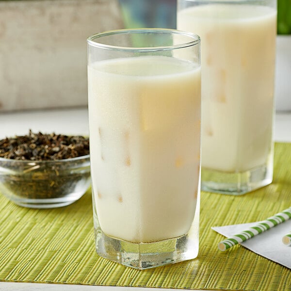 A glass of iced jasmine green tea with milk on a green placemat, with a bowl of loose leaf tea in the background.