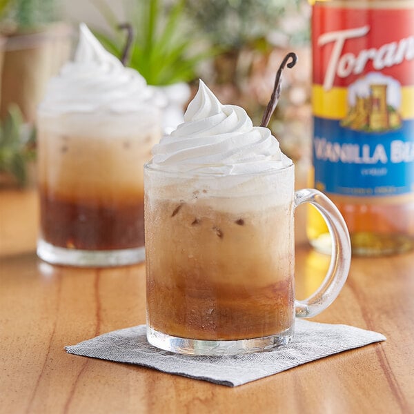 A glass mug with a brown drink and whipped cream on top.