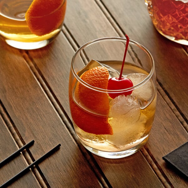 A glass of Master of Mixes Old Fashioned drink with ice, an orange slice, and a cherry.