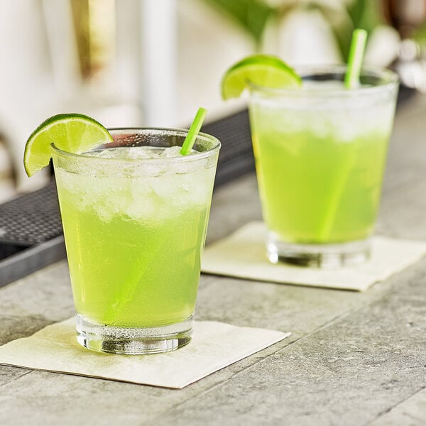 Two glasses of green DaVinci Gourmet Sweetened Lime cocktail with lime slices on a table in a cocktail bar.