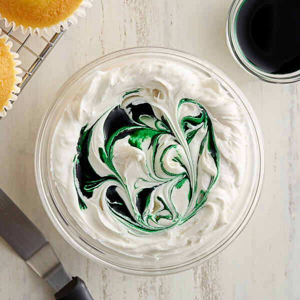 A bowl of white frosting with a green swirl on a cupcake.