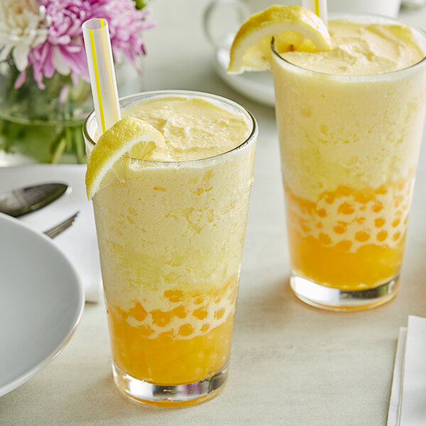 Two glasses of yellow liquid with straws and lemon slices on a table