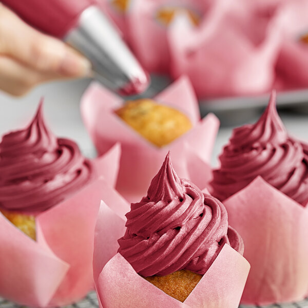 A close-up of a cupcake with pink frosting and a brown wrapper.