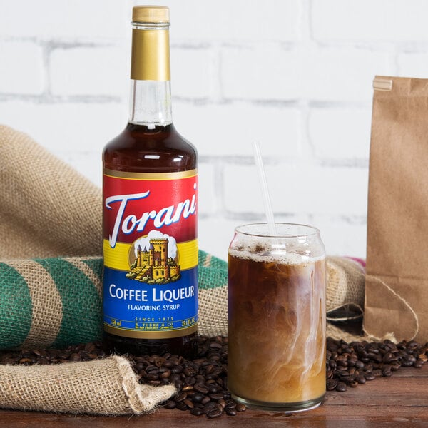 A Torani Coffee Liqueur Flavoring Syrup bottle next to a glass of coffee syrup.