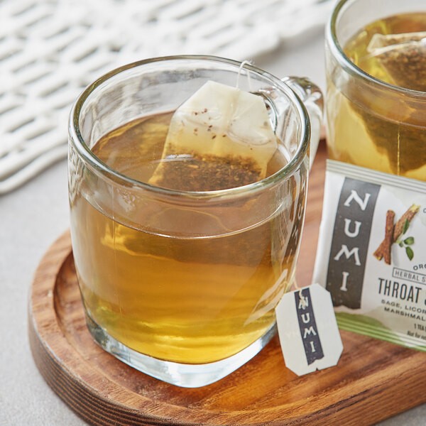 A glass mug of Numi Organic Throat Soother Herbal Tea with a tea bag in it.