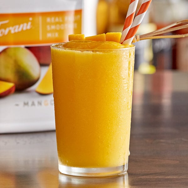 A glass of mango smoothie with a straw next to a bag of mangoes.