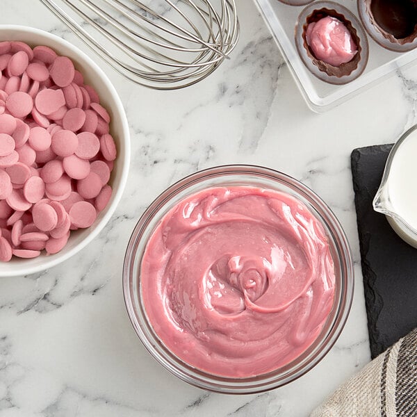 A bowl of pink frosting with Callebaut Ruby chocolate chips and a whisk.