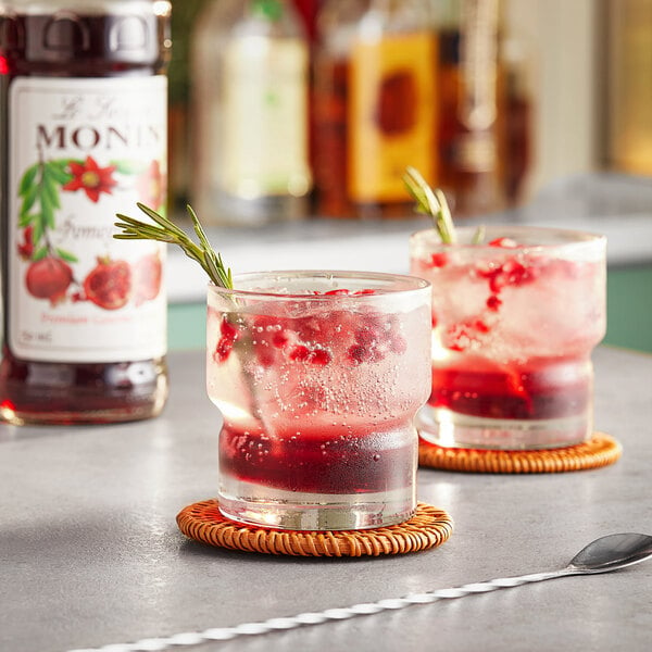 Two glasses of red liquid with Monin Pomegranate Flavoring on a table.