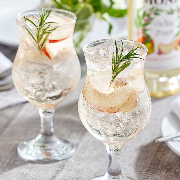 Two glasses of Monin White Peach flavoring with ice and fruit on a table.