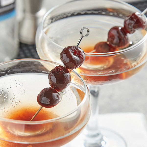 A pair of martinis with Fabbri Amarena cherry skewers on a table in a cocktail bar.