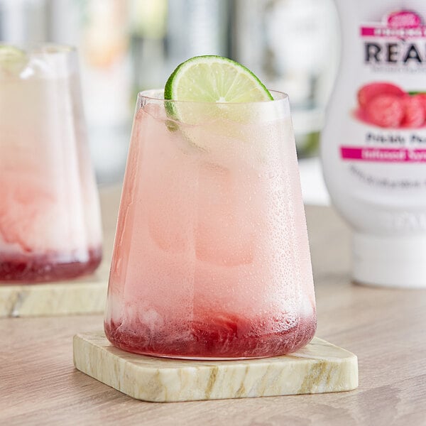 A glass of pink liquid with a lime wedge on the rim.