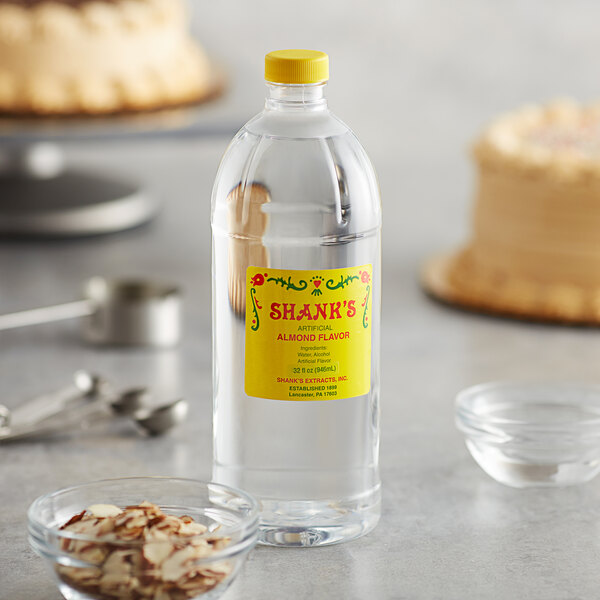 A close up of a bottle of Shank's Imitation Almond Extract on a table next to a cake.