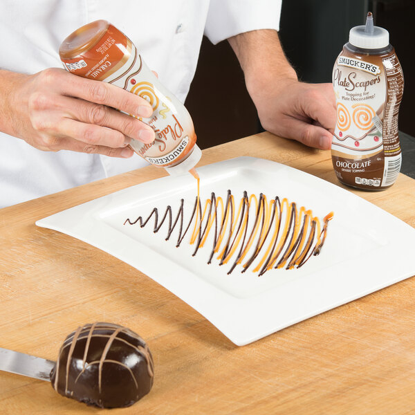 A person pouring caramel sauce on a chocolate dessert with a crisscrossed design using a Smucker's Caramel Platescapers bottle.