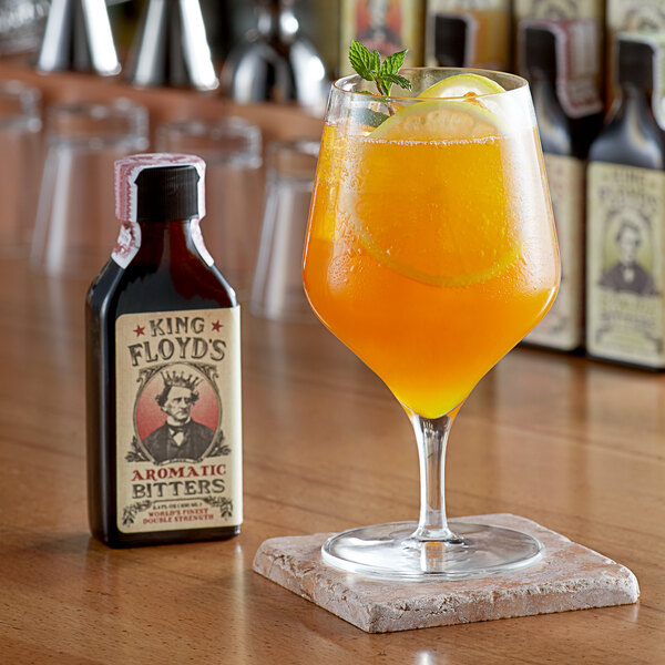 A glass of orange liquid with lemons and mint in front of a bottle of King Floyd's Aromatic Bitters.