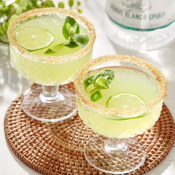 Two glasses of Lyre's Agave Blanco non-alcoholic tequila with limes and mint leaves.