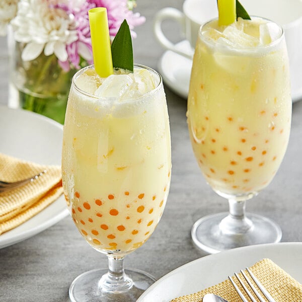 Two glasses of yellow Fanale pineapple bubble tea with straws and green leaves.